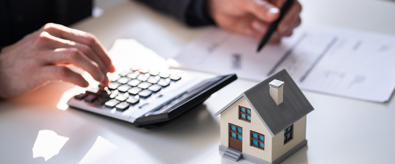 A male hand using a calculator while a wooden figure of a property sits on the desk